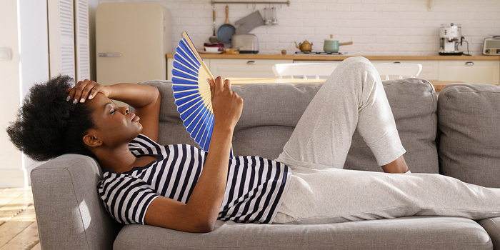 woman laying down on couch fanning herself to cool off